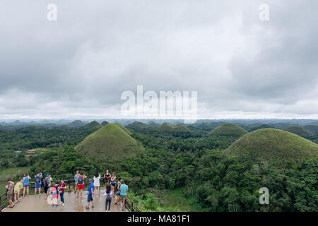 A young group of male and female tourists standing on the viewing platform over looking the famous Chocolate Hills landmark in Bohol province of the P Stock Photo