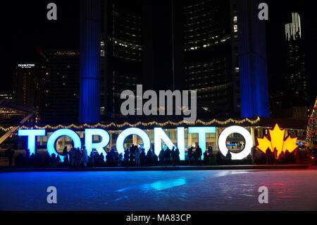 TORONTO, CANADA - 2018-01-01 : People in front of TORONTO sign with Christmas tree in the night viewed across the skating rink on the central Nathan P Stock Photo