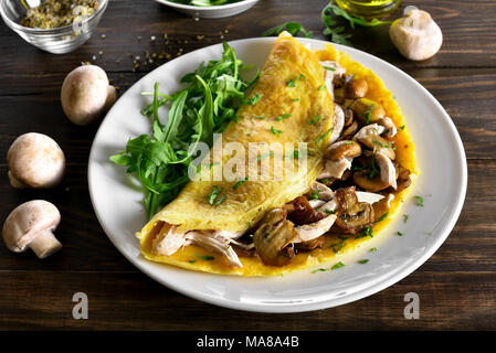 Close up of omelet with mushrooms, chicken meat, greens on wooden table. Healthy food for breakfast. Stock Photo