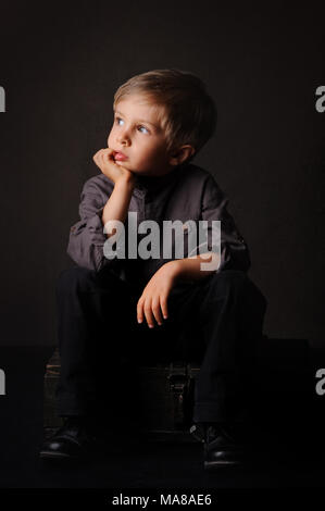 A five years old pensive boy portrait, studio shot, dark background, indoor waist up portrait, head leaning hand, Stock Photo