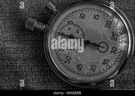 Stopwatch on worn jeans background, value measure time, old clock arrow minute and second accuracy timer record. Stock Photo