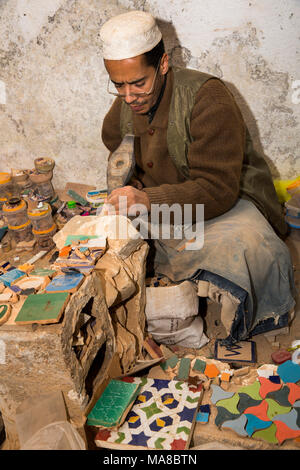Morocco, Fes, Quartier des Potiers, Pottery, worker hand cutting zellij patterned decoration tiles Stock Photo