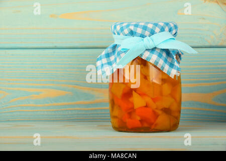 Close up of one glass jar of homemade quince jam with textile top decoration and ribbon bow at blue painted vintage wooden planks background, low angl Stock Photo