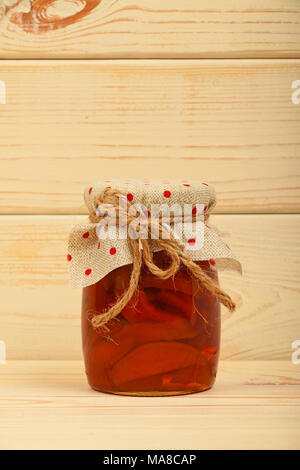 Close up of one glass jar of homemade quince jam with textile top decoration and twine bow over white beige painted vintage wooden planks background,  Stock Photo