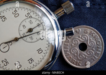 Denmark coin with a denomination of five krone (crown) and stopwatch on dark blue jeans backdrop - business background Stock Photo