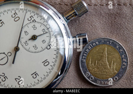 Thai coin with a denomination of ten baht and stopwatch on old beige denim backdrop - business background Stock Photo