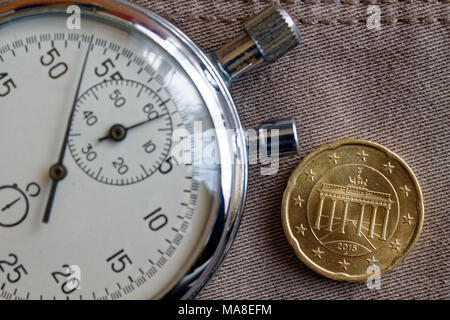 Euro coin with a denomination of 20 euro cents (back side) and stopwatch on beige denim backdrop - business background Stock Photo