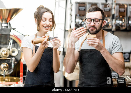 Couple of baristas in uniform checking the quality of roasted coffee beans standing near the roaster machine Stock Photo