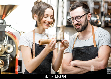 Couple of baristas in uniform checking the quality of roasted coffee beans standing near the roaster machine Stock Photo