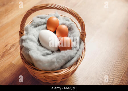 Goose egg and hens eggs, in a basket on soft fluffy wool, with a wooden floor background. Stock Photo