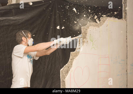 A young man breaks a partition in the apartment with a hammer Stock Photo