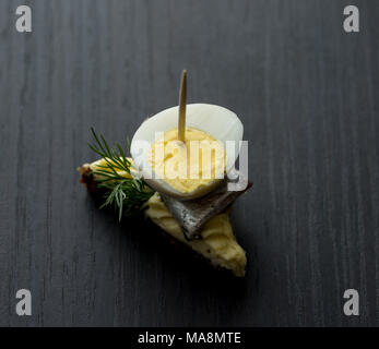 Mini sandwich with salt sprat and sliced boiled quail egg on the slice of bread. Canned fish is Estonian national food.   Concept of food and organic  Stock Photo