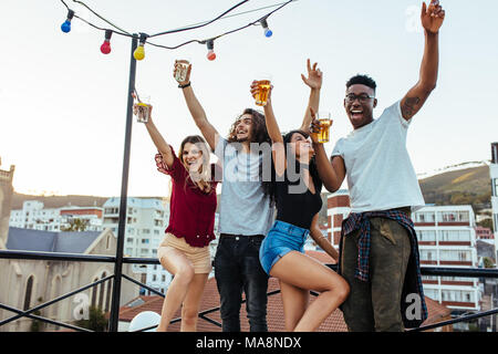 Friends enjoying and having fun at rooftop. Multiracial men and woman having party on rooftop in evening. Stock Photo