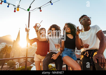 Group of young friends having fun, drinking and enjoying a evening on rooftop. Multiracial men and woman hanging out at rooftop party in evening. Stock Photo