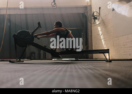 Female athlete using rowing machine. Fit woman doing cardio workout in fitness gym. Stock Photo