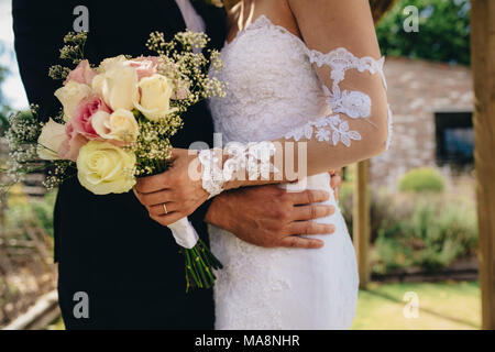 Mid section of couple standing together on their wedding day. Bride and groom with a flower bouquet. Stock Photo