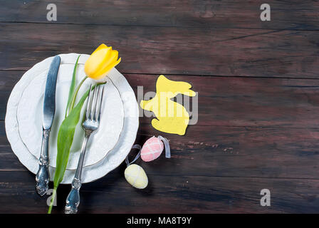 Place Setting for Easter, olored easter eggs and  bouquet of yellow tulips on a wooden background Stock Photo