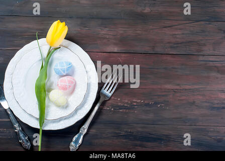 Place Setting for Easter, olored easter eggs and  bouquet of yellow tulips on a wooden background Stock Photo