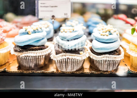 Macro closeup of chocolate cupcakes on display in bakery in muffin paper liners with blue blueberry icing cream Stock Photo
