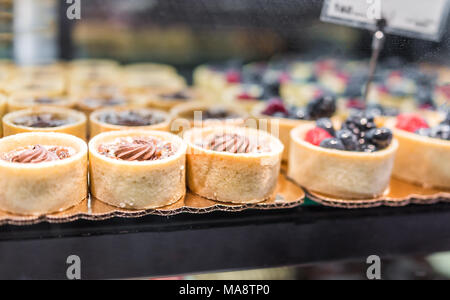 Macro closeup of chocolate chestnut pastry baked mini small crust golden tarts on display in gourmet bakery, frosting, berry Stock Photo