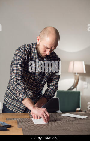 Cutting wool fabric. the line pattern. Bow ties of woolen fabric. Young man working as a tailor and using a sewing machine in a textile studio. Stock Photo