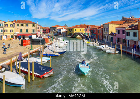 Murano, Italy - October 07, 2017: View across San Donato channel with colorful houses, multiple moored boats and single small boat moving in the water Stock Photo