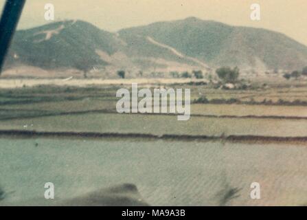 Color photograph, shot from inside a vehicle, showing a flat expanse of rice paddies, with mountains in the distance, photographed in Vietnam during the Vietnam War, 1968. () Stock Photo