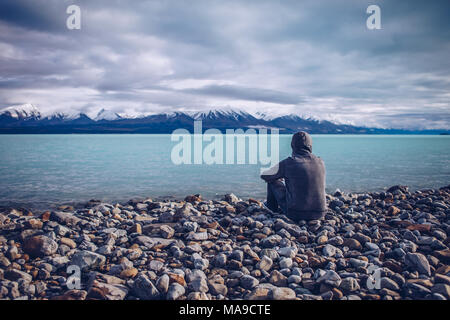 Young man looking out over Lake Tekapo and snow capped mountains in New Zealand