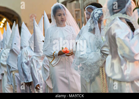 Queretaro, Mexico, 31 Mar 2018. A young girl dressed in white carries a single rose during the Procession of Silence through the streets on Good Friday during Holy Week March 30, 2018 in Querétaro, Mexico. Hooded penitents, known as Nazarenes, and young girls symbolizing the Virgin Mary process through the streets of the city to recreate the passion of Christ. Credit: Planetpix/Alamy Live News Stock Photo