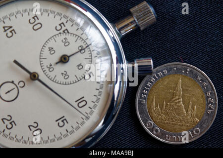 Thai coin with a denomination of ten baht and stopwatch on old worn black denim backdrop - business background Stock Photo