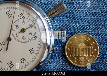 Euro coin with a denomination of 20 euro cents (back side) and stopwatch on worn jeans backdrop - business background Stock Photo