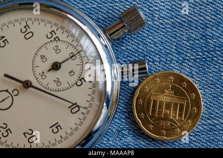 Euro coin with a denomination of 20 euro cents (back side) and stopwatch on blue denim backdrop - business background Stock Photo