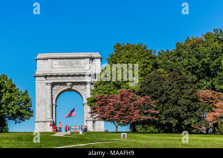 A bold, bright summer's day view of the Valley Forge National Memorial Arch framing an American flag, with tourists, colorful trees and copyspace. Stock Photo