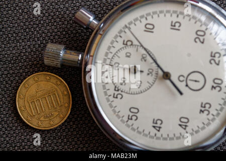 Euro coin with a denomination of 10 euro cents (back side) and stopwatch on brown denim backdrop - business background Stock Photo