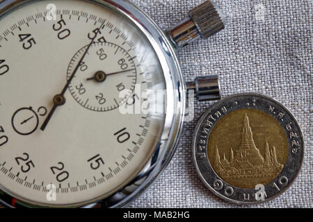 Thai coin with a denomination of ten baht (back side) and stopwatch on linen backdrop - business background Stock Photo