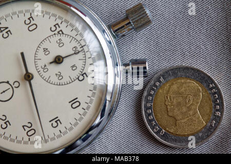 Thai coin with a denomination of ten baht (back side) and stopwatch on gray denim backdrop - business background Stock Photo