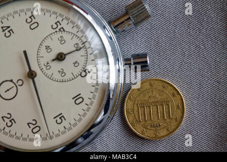 Euro coin with a denomination of 10 euro cents (back side) and stopwatch on gray denim backdrop - business background Stock Photo