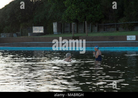 Two women in a large ocean pool chatting just on dawn at Forster on the mid north coast of New South Wales, Australia Stock Photo