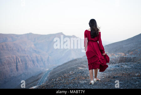Fashionable girl on a desert mountain top wearing red dress Stock Photo