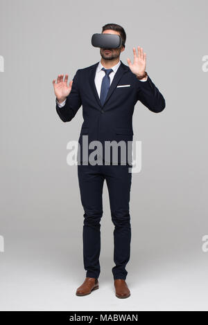 Stylish businessman in formal wear using VR glasses, touching imaginary virtual interface Stock Photo