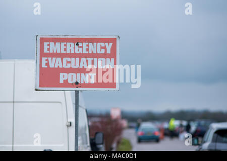 red emergency evacuation point sign with cars leaving in background Stock Photo