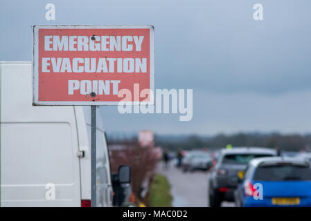 red emergency evacuation point sign with cars leaving in background Stock Photo