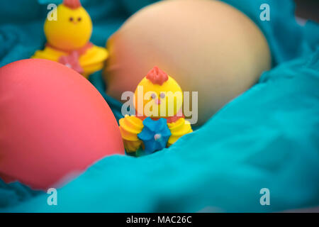 Three toy chickens and three easter eggs on the grass in a blue basket. Composition. Stock Photo