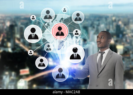 Businessman works on a touch people connection icon on screen interface with cityscape background. Stock Photo