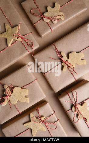 Plain wrapped Christmas presents tied with twine and decorated with holiday shaped cookies, flat lay shot from above. Stock Photo