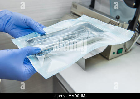 Close up dentist assistant's hands holding packaged with vacuum packing machine medical instruments ready for sterilizing in autoclave. Dental office. Selective focus, space for text. Stock Photo