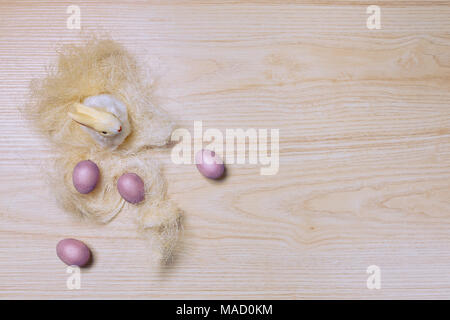 Easter decorations on wooden background with grass, rabbit and eggs. Top view. Pastel colours. Stock Photo