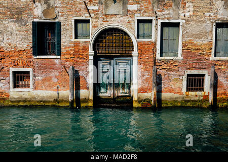 Facade of partially mossy old brick house with wooden vintage door on narrow canal in Venice, Italy. Stock Photo