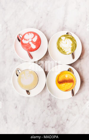 Four different colored latte coffee, style of foam art, natural organic beverages in modern cafe on white marble background Stock Photo