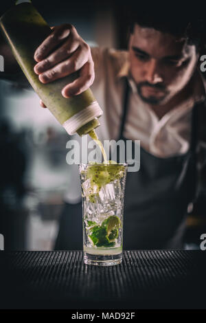 Barman pouring sweet syrup into the fresh sour lime and kiwi cocktail on the bar counter Stock Photo